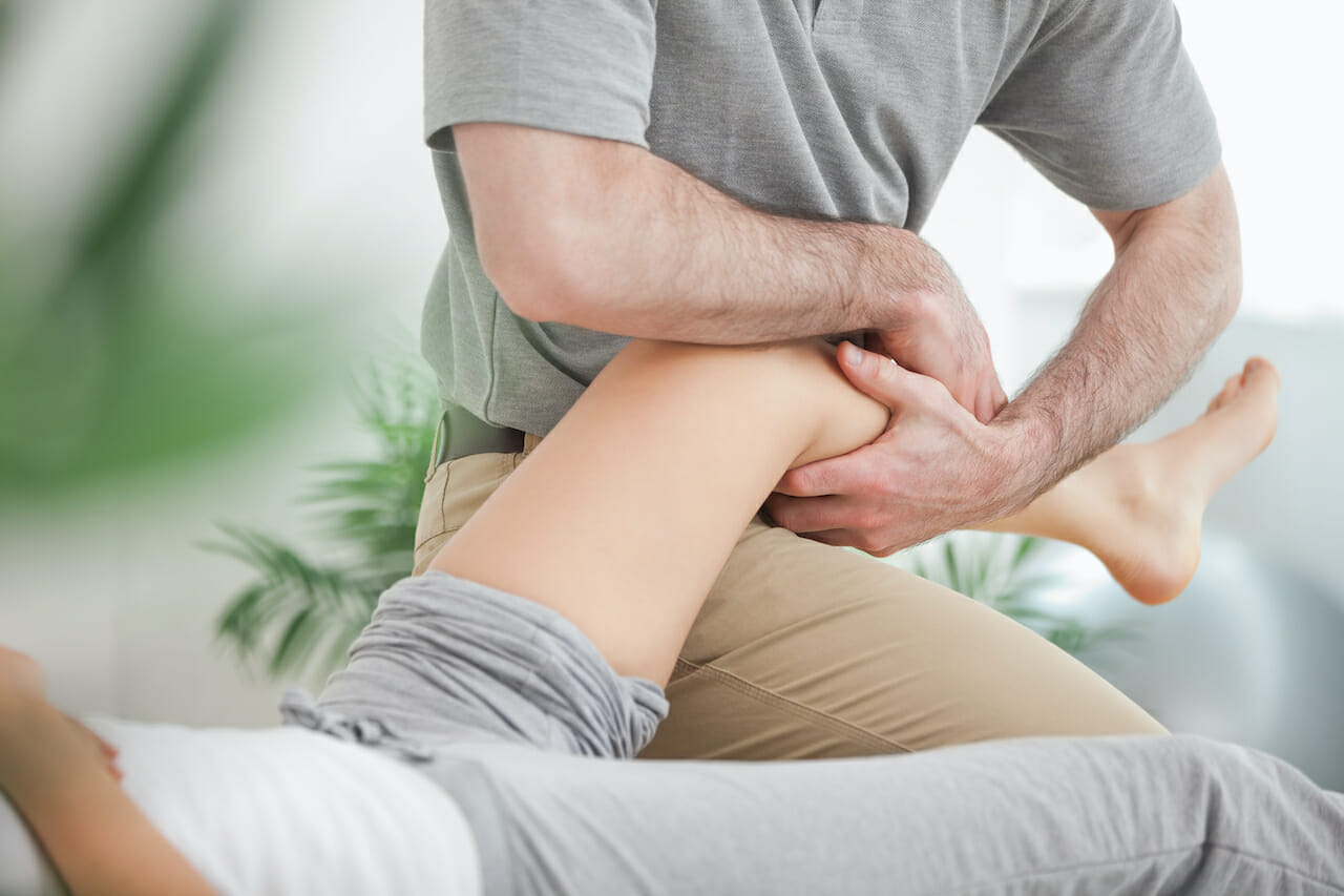 Man manipulating the leg of a woman while she is lying in a room